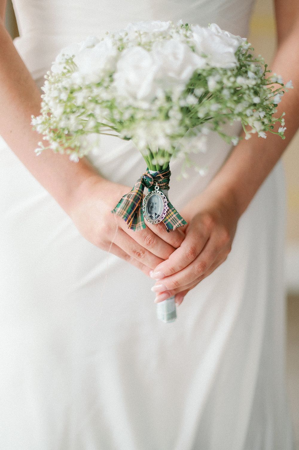 A delicate white and green bridal bouquet wrapped with tartan ribbon held by hands in a white dress.