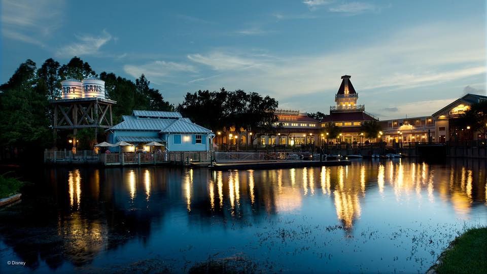 Evening panorama of illuminated buildings reflecting on water at Disney's Port Orleans Resort.