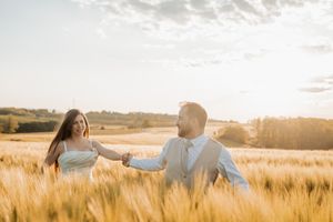 Pár sétál egy aranyló búzamezőn naplementekor, a meleg napfény sziluetteket és lencsefényt hoz létre.