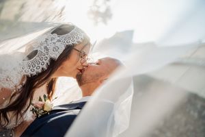 Bride and groom share a romantic kiss under a flowing lace veil on their wedding day.