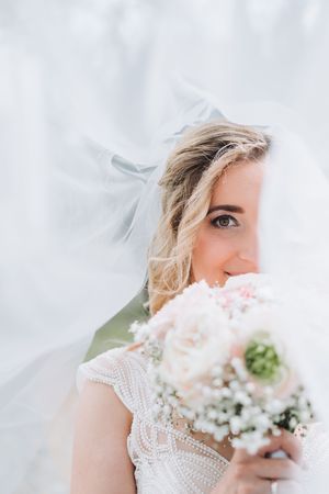 Bride holding a bouquet of pink and white flowers, partially covered by a flowing white veil on her wedding day.