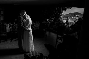Black and white wedding photo of bride and groom embracing on a terrace with scenic hills in the background.