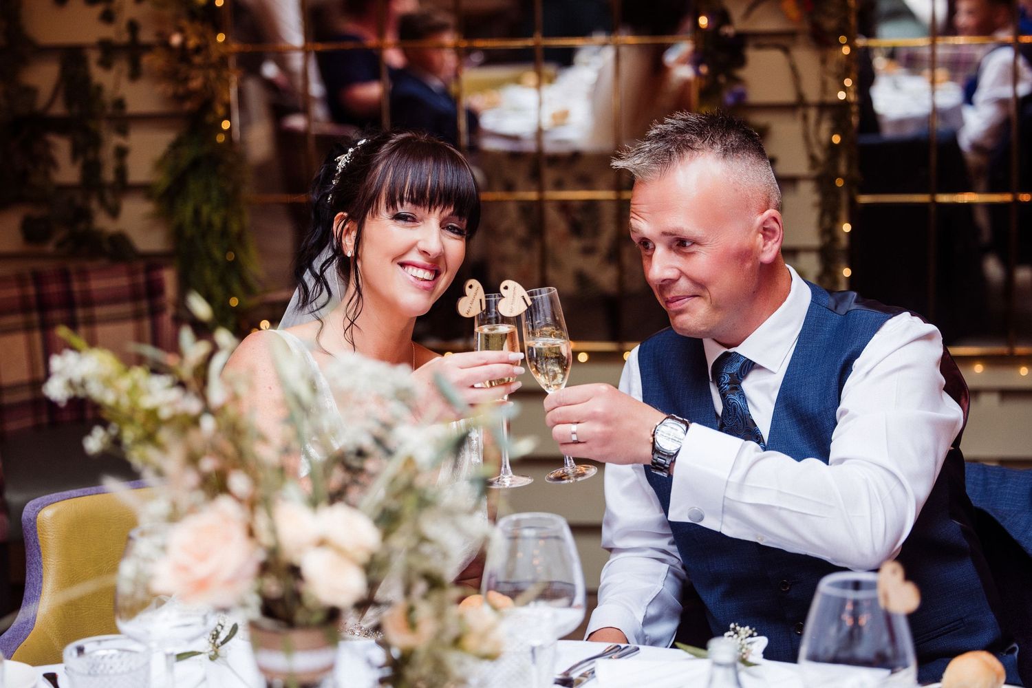 Couple toasts with champagne glasses while sitting at an elegantly decorated wedding reception table.