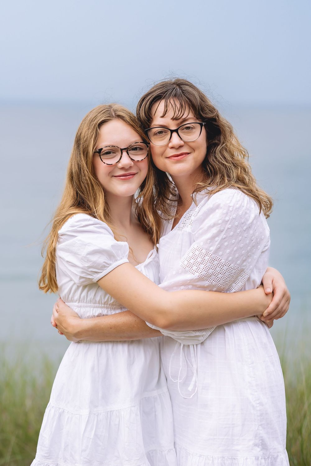 Two people in white dresses share loving embraces while posing outdoors in a natural setting.