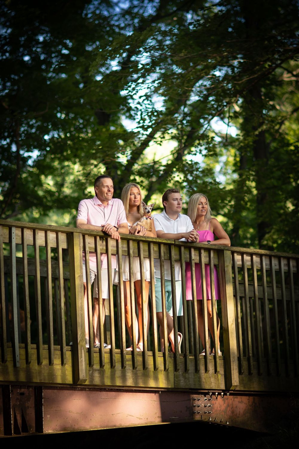 Family members lean against wooden bridge railing during outdoor photo session.
