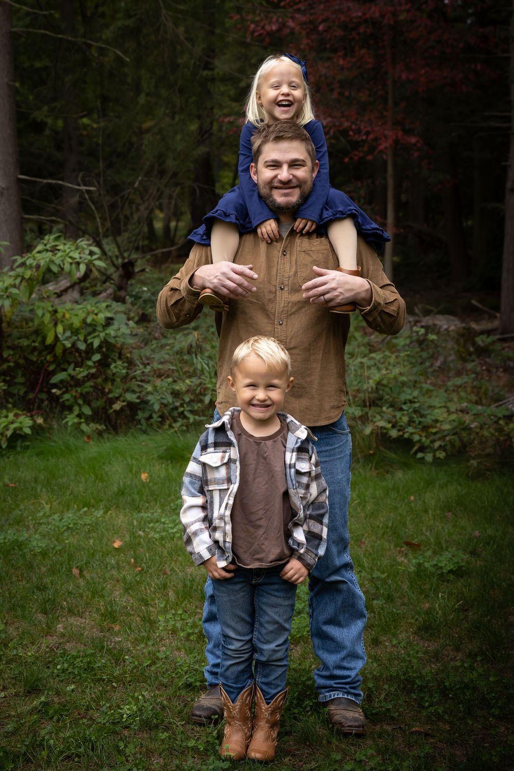 Two young children in casual clothing playing and hugging outdoors in a wooded setting.