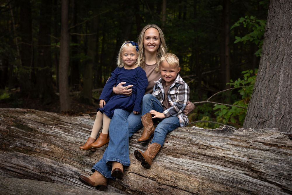Family sits together on a large fallen log in a peaceful forest setting.