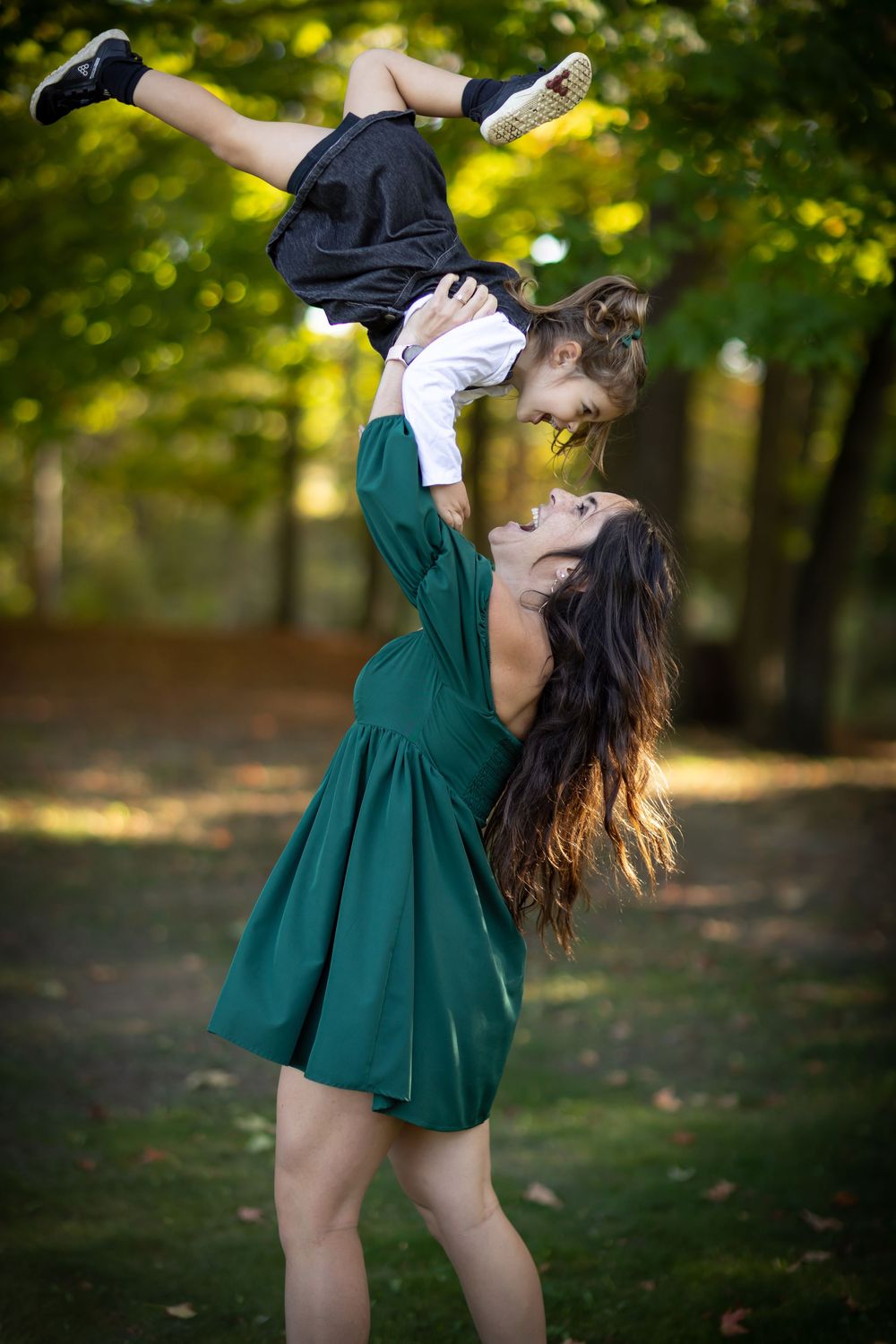Woman in emerald dress performs energetic dance moves in a park with autumn trees in the background.