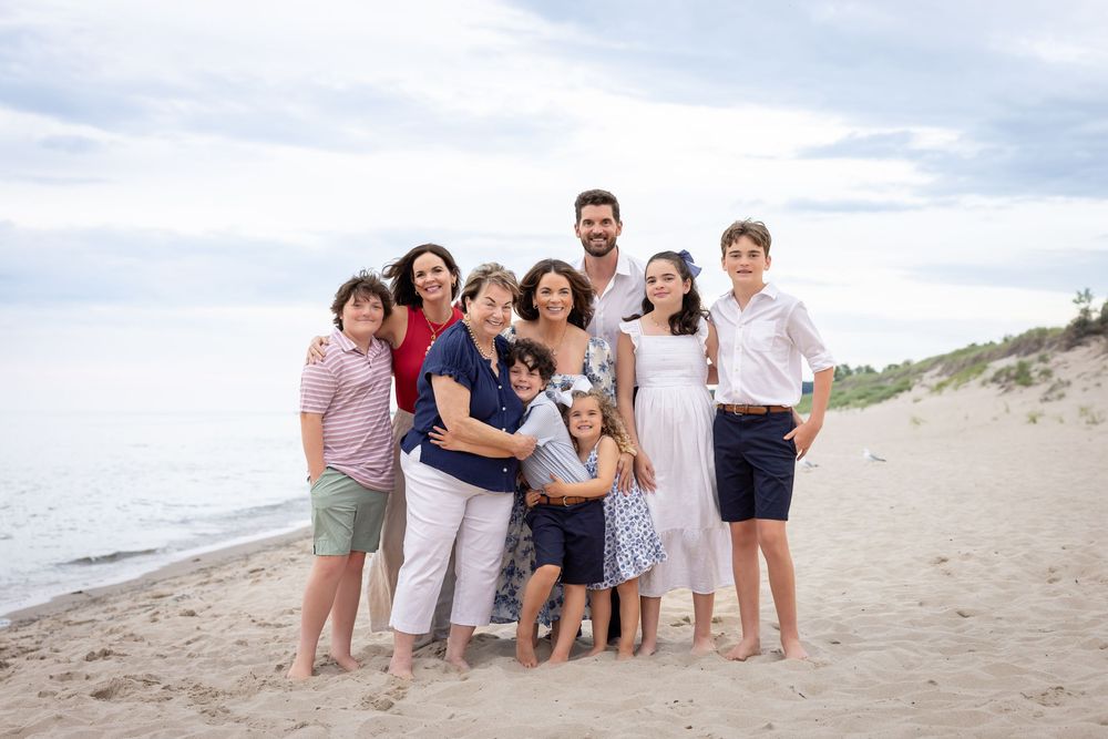 Group of people posing together on a sunny beach with sand dunes in the background.