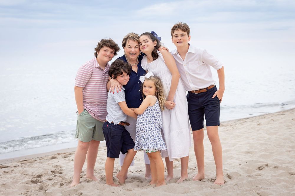 Family group gathered together on sandy beach with ocean waves visible behind them.
