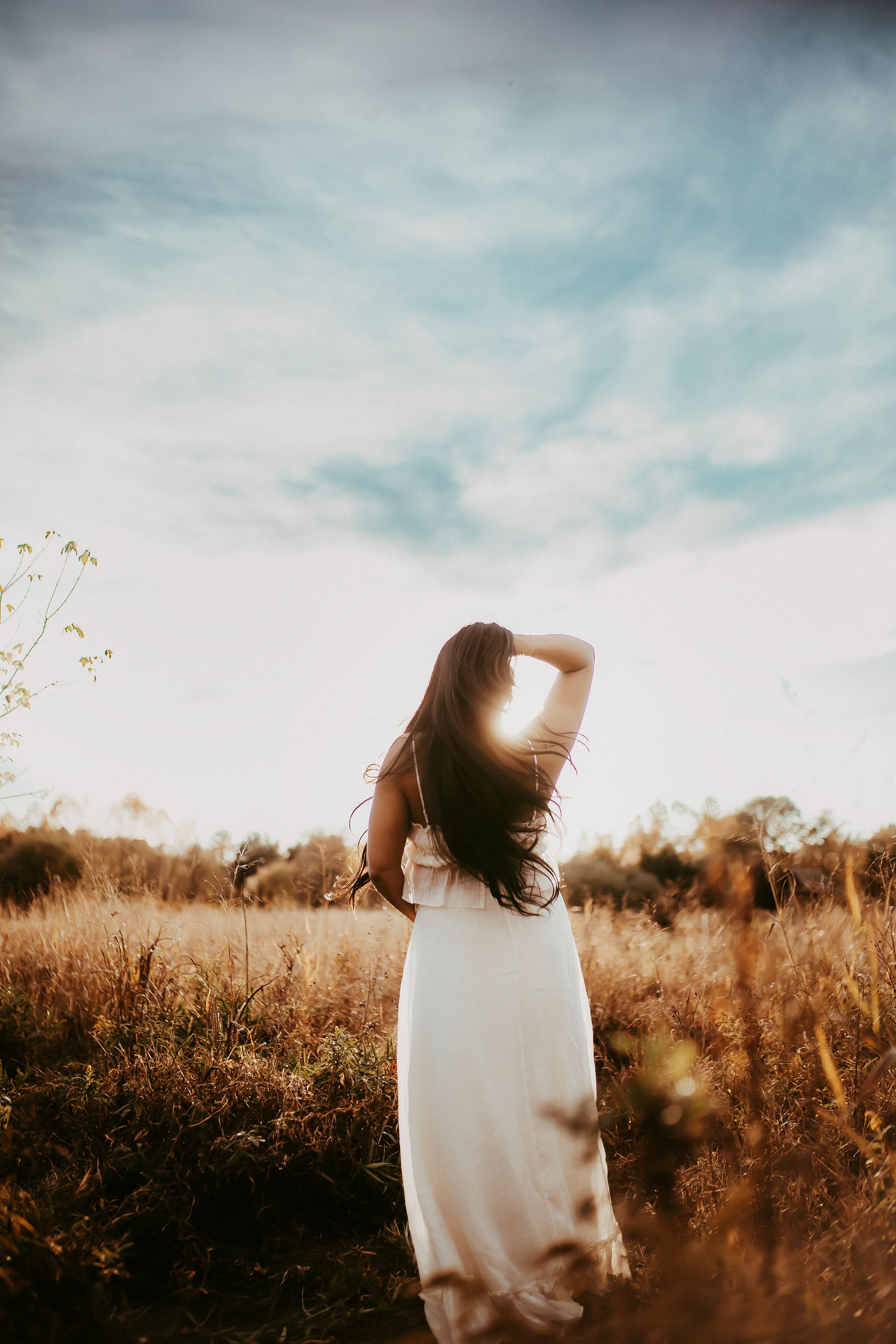 Person in white dress standing in golden field at sunset.