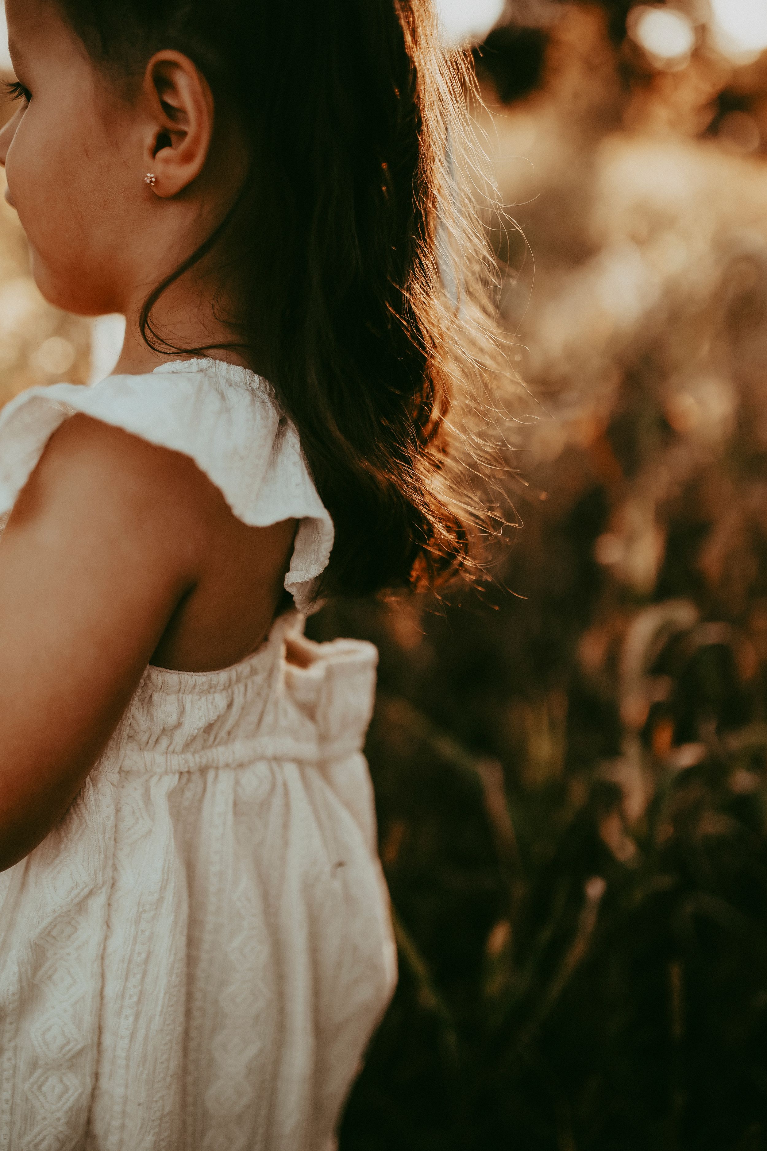 Child wearing white ruffled dress captured in golden sunset light.
