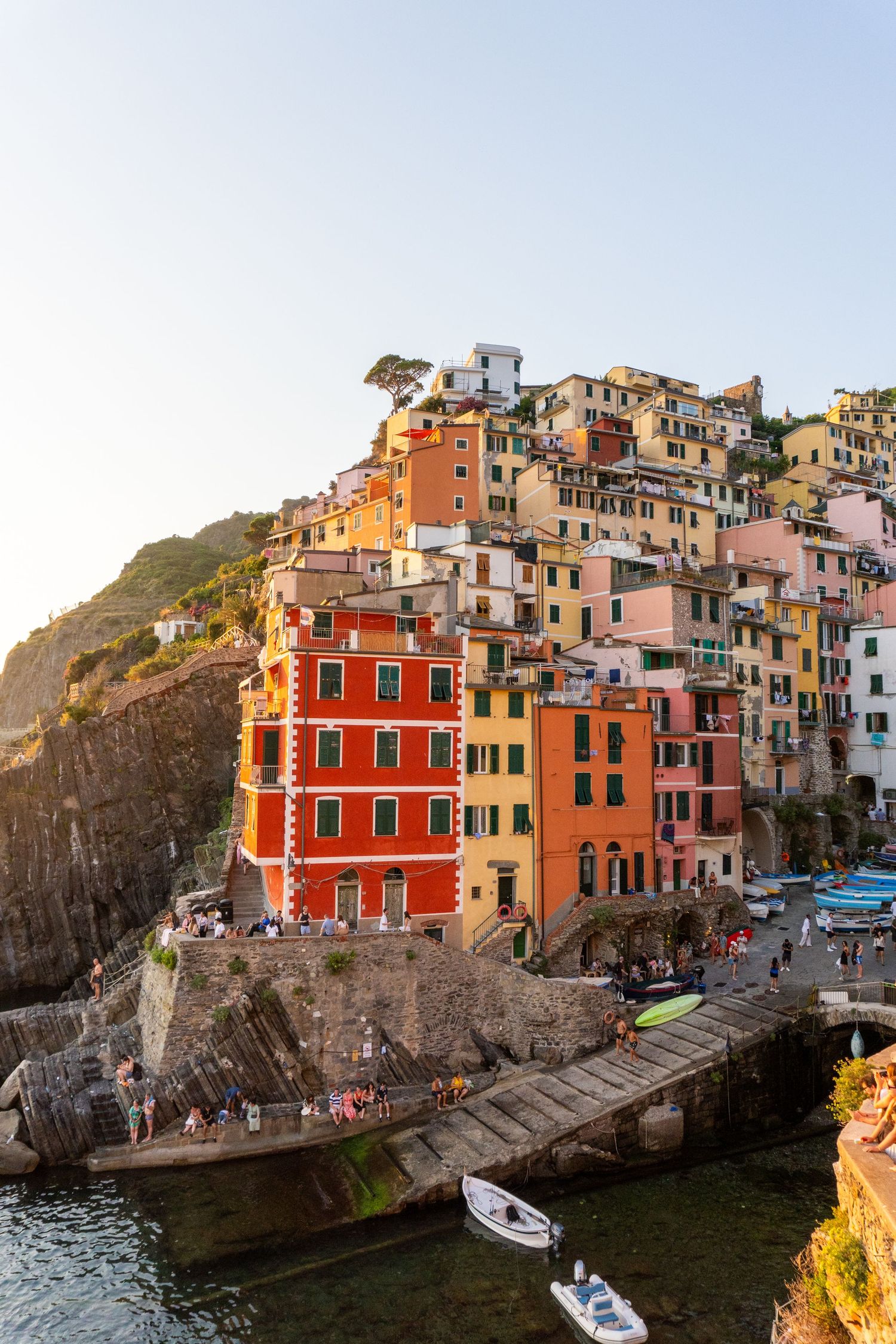 Colorful buildings of Cinque Terre perched on cliffs above the Mediterranean Sea with small boats in the harbor at sunset.