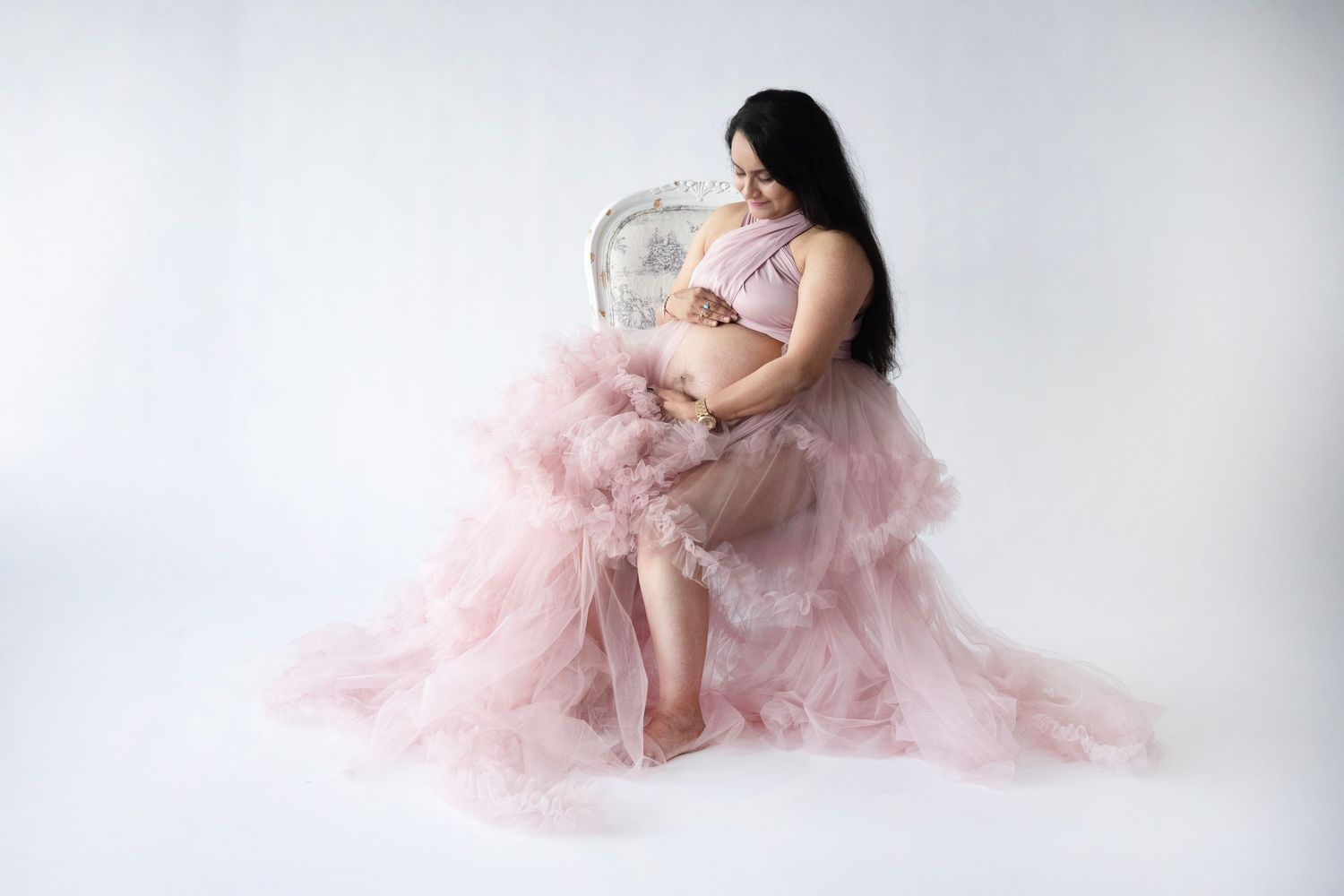 Ethereal maternity photoshoot featuring flowing pink tulle gowns against a white backdrop.