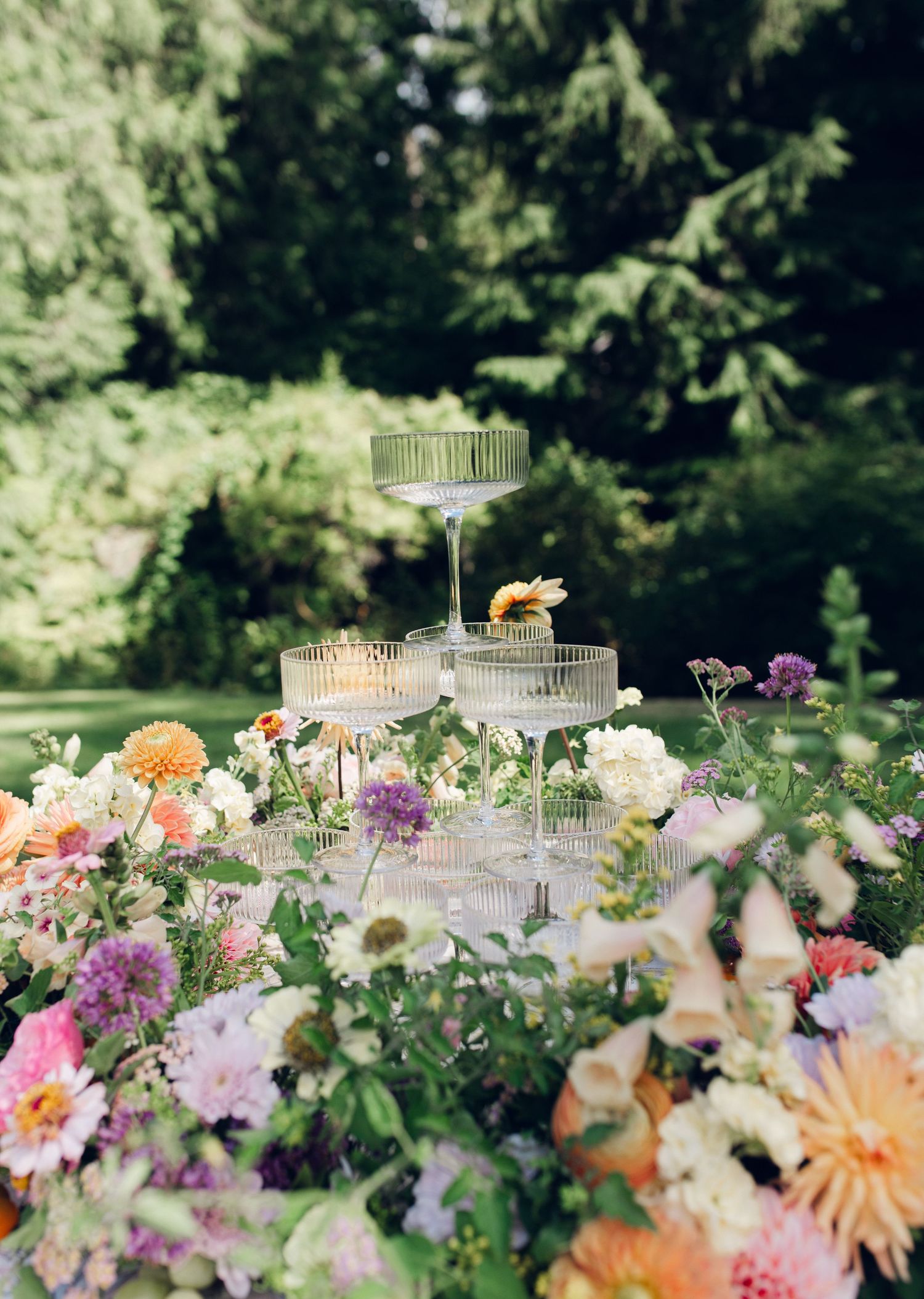 Elegant outdoor table setting with crystal cake stands and delicate floral arrangements in peach and purple tones.