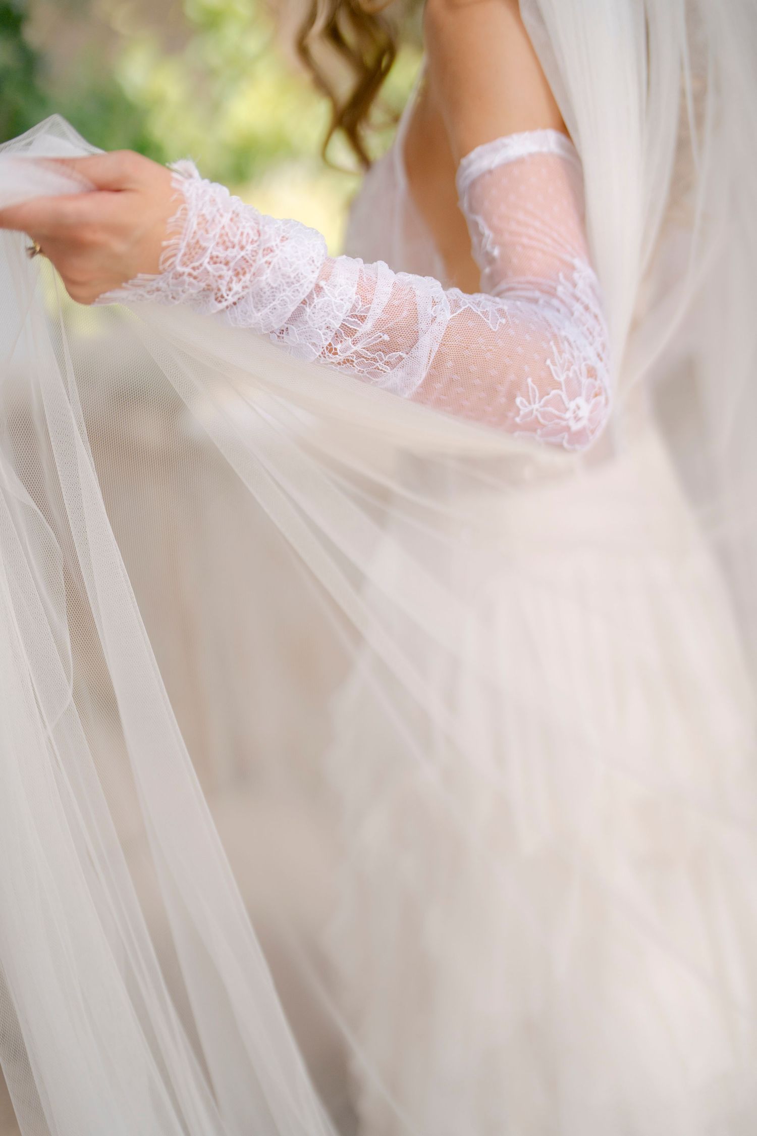 Close-up details of delicate white lace sleeves and flowing tulle fabric from a romantic wedding dress.