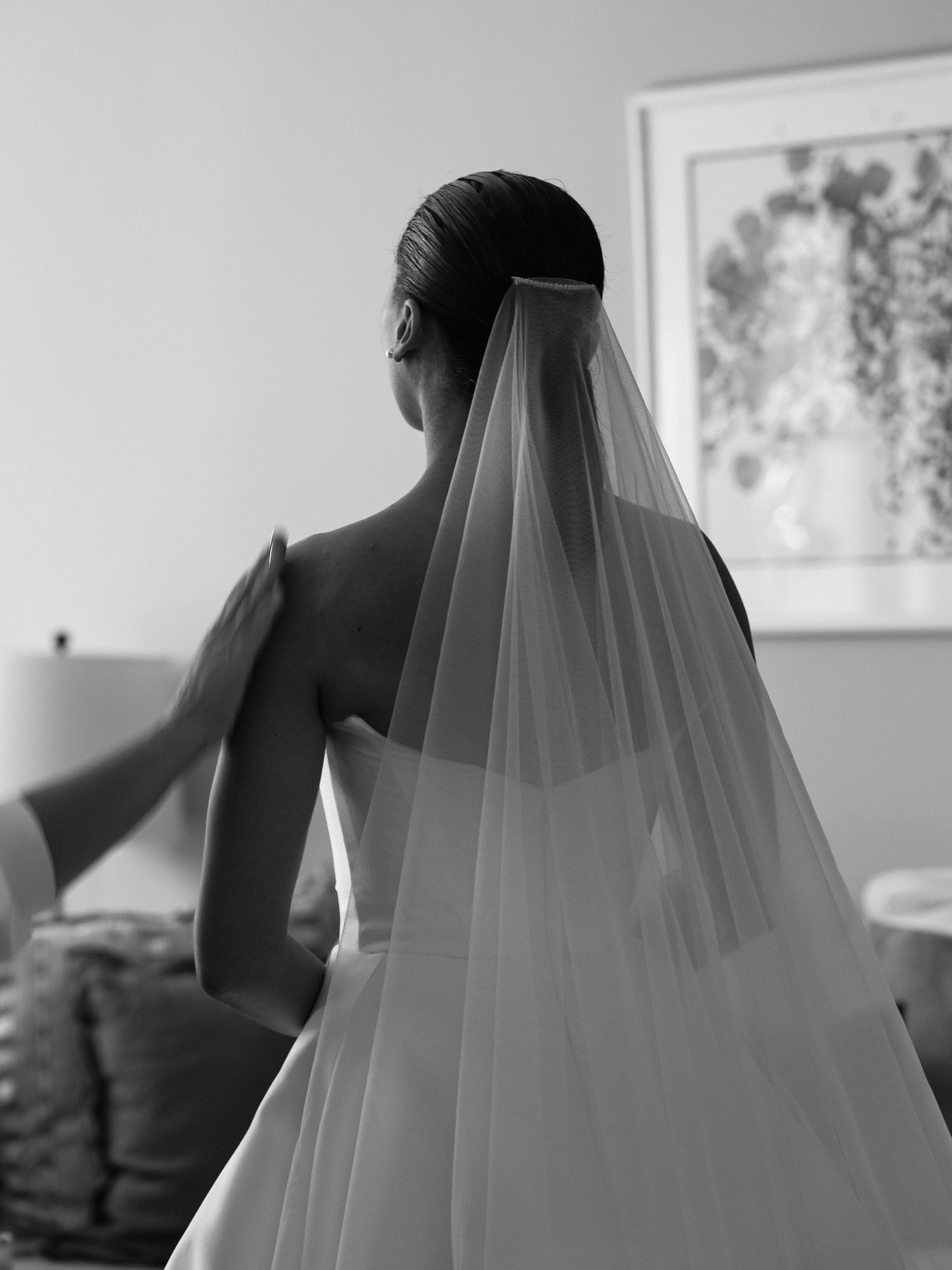 A black and white photo shows the back view of a bride wearing a flowing veil and strapless gown.