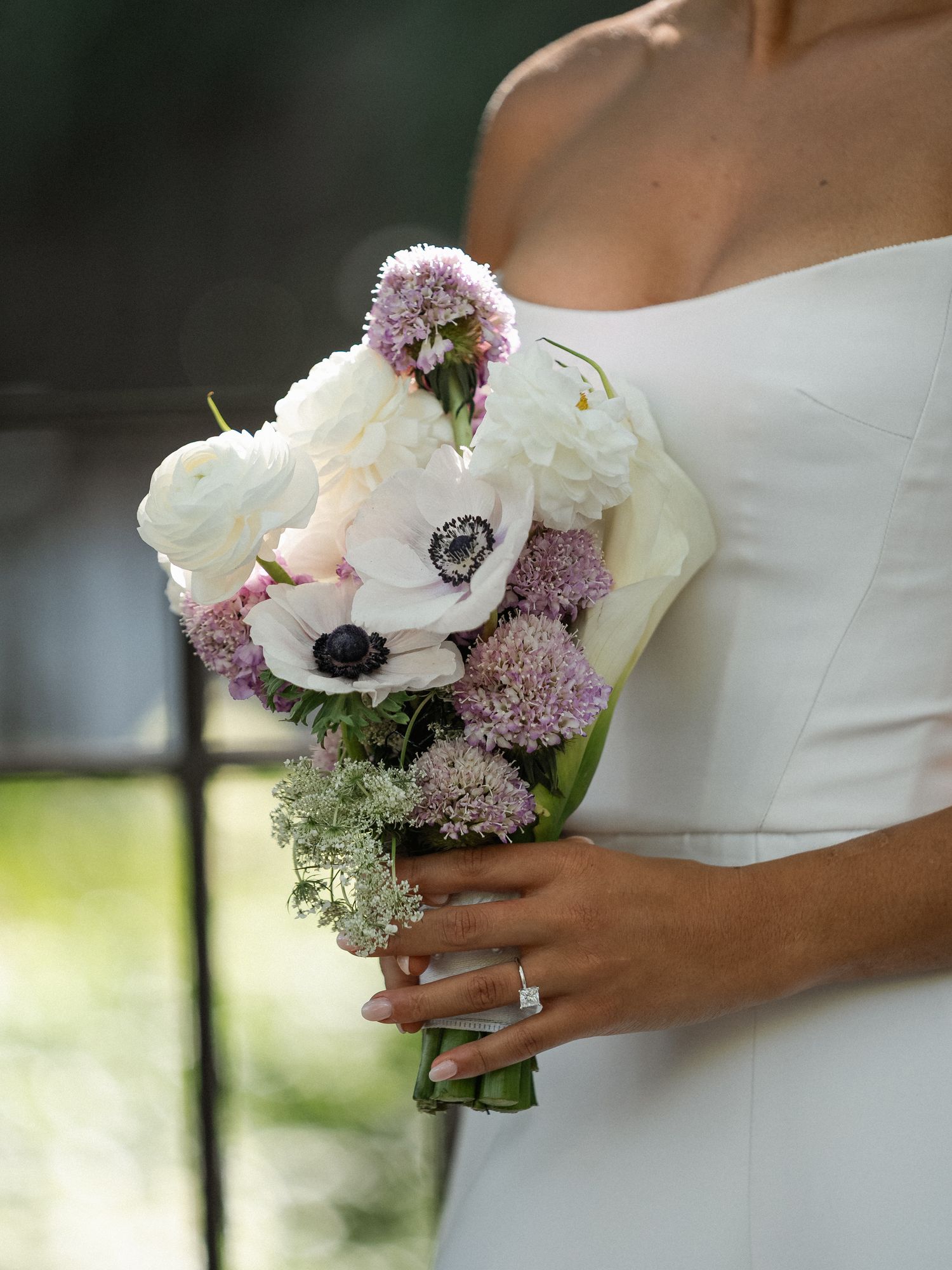 An elegant bridal bouquet features white anemones, purple lilac, and delicate greenery.