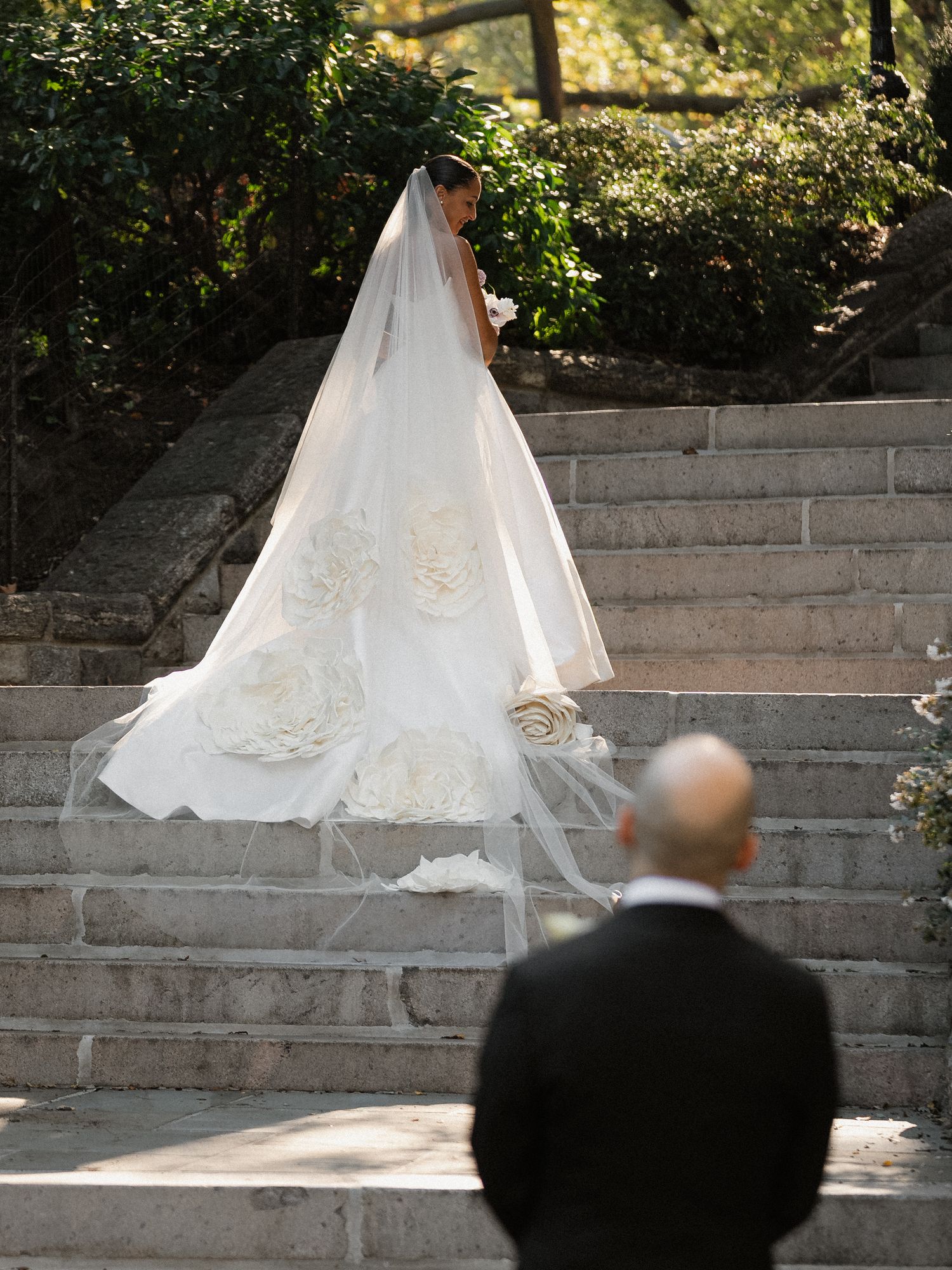 Wedding dress train flows elegantly down stone steps in garden setting.