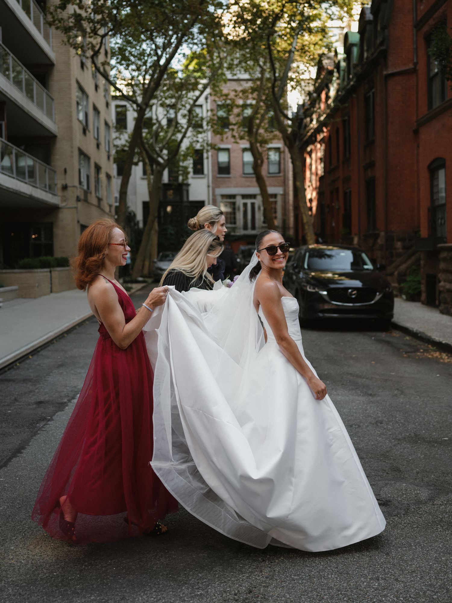 A wedding party helps with the bride's dress on a charming city street.