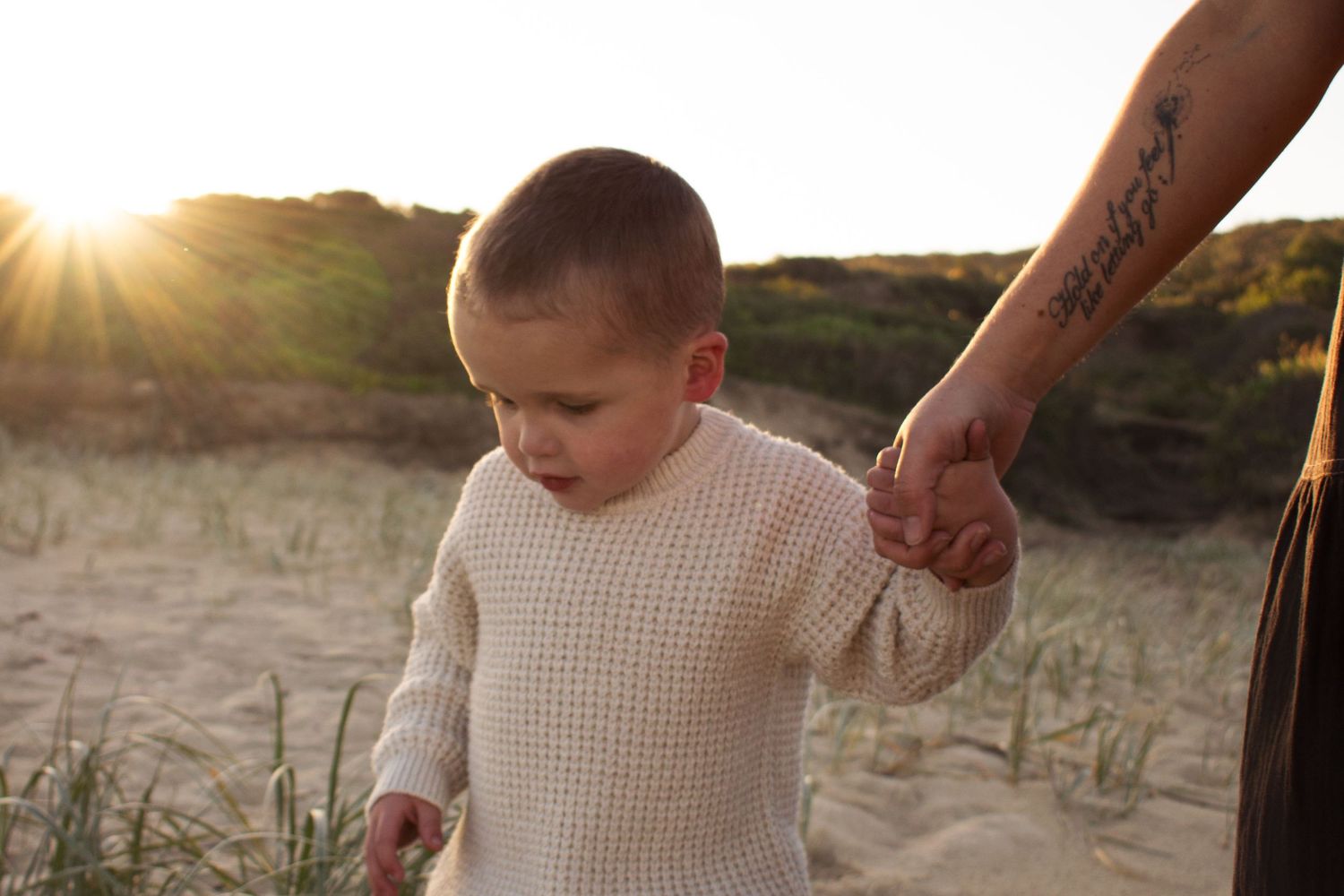 toddler holding his mums hand as he watches where he walks at a golden hour motherhood beach photoshoot Dudley beach Newcastle NSW