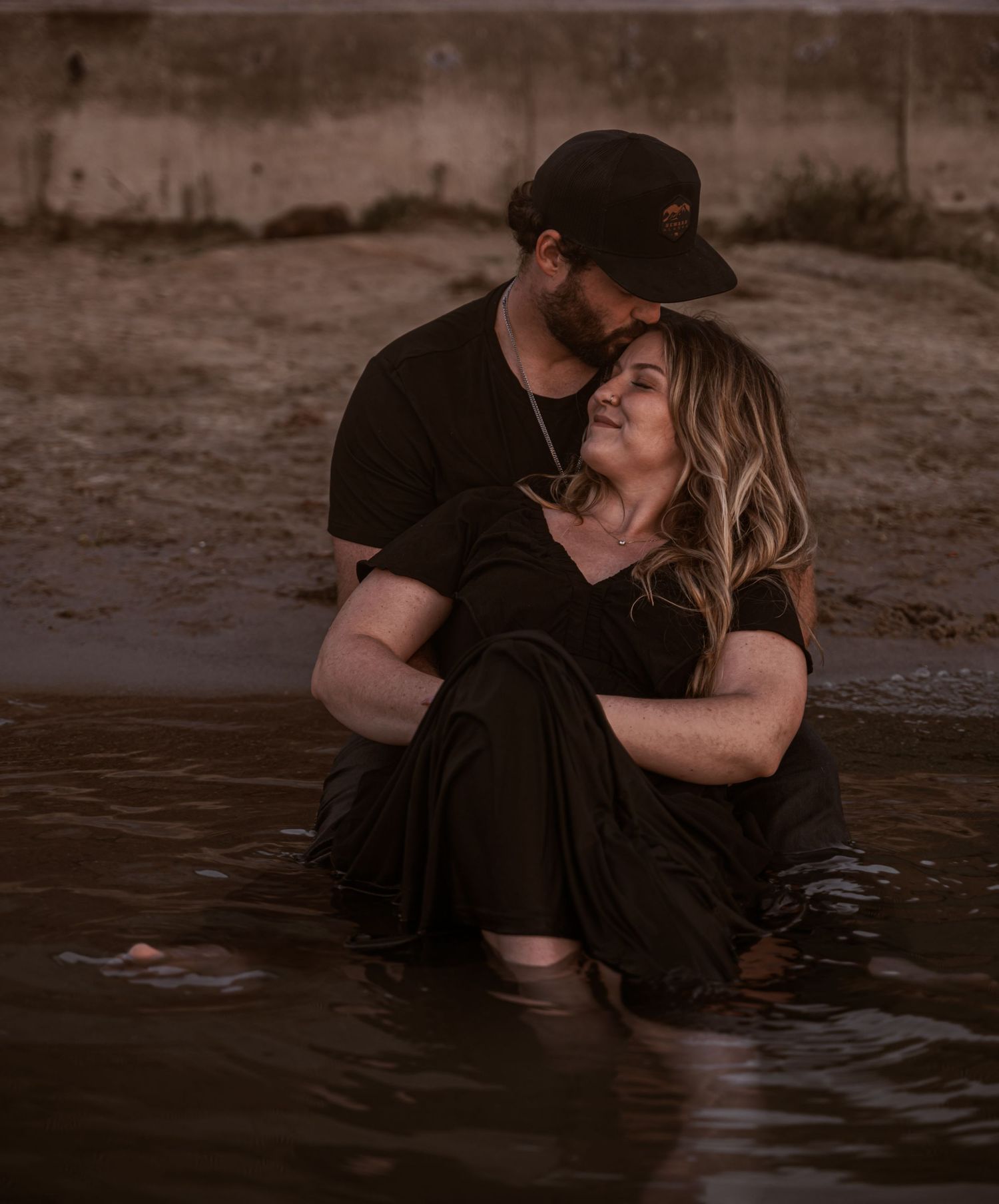 A couple shares an intimate moment while sitting in shallow water at sunset, creating a romantic silhouette.
