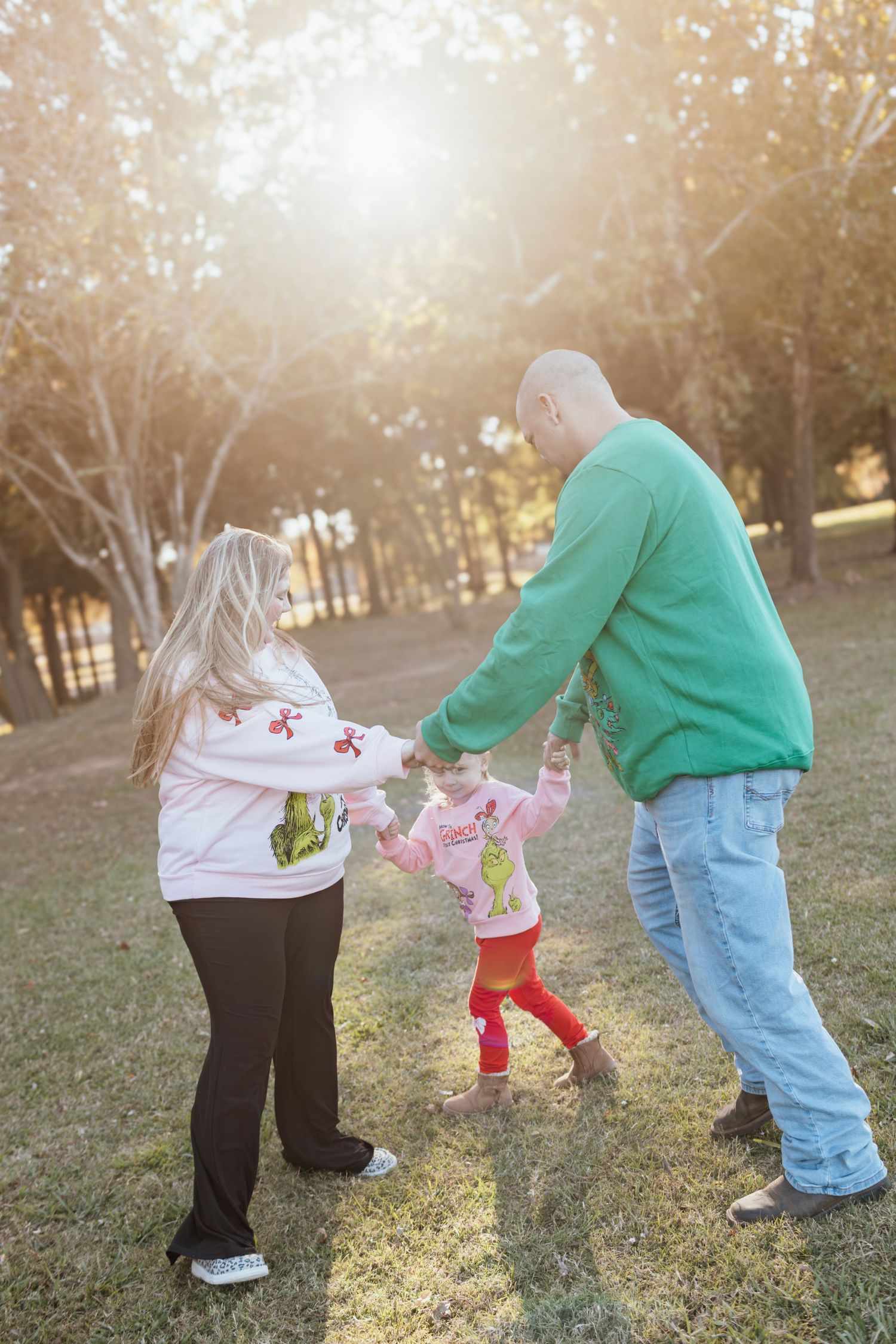 Three people in casual clothing play together on grass during golden hour sunlight.