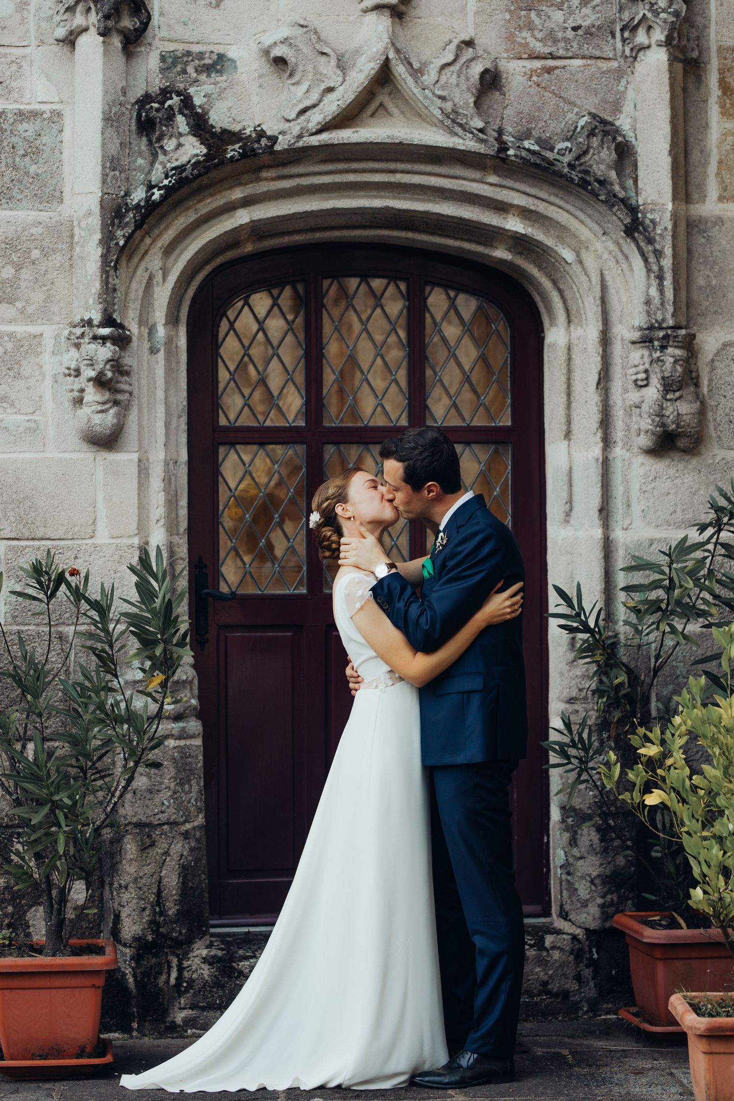 Bride and groom kissing in front of ornate Gothic stone doorway of historic European building.