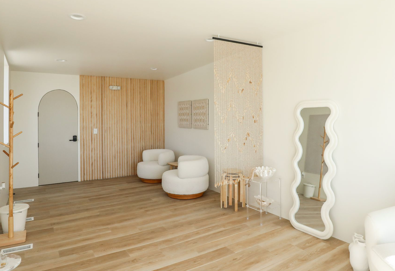 Modern minimalist room interior with light wood flooring, white walls, curved doorway and contemporary furniture pieces.
