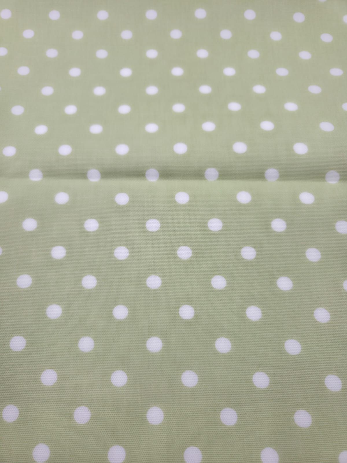 White polka dots pattern on a soft sage green cotton fabric background creates a classic retro design.