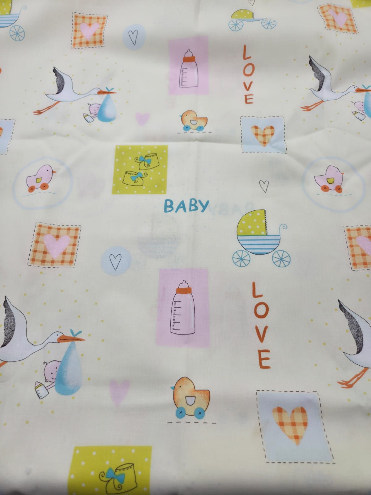 Baby-themed fabric pattern with storks, bottles, hearts, and 'LOVE' text on light background for nursery decor.