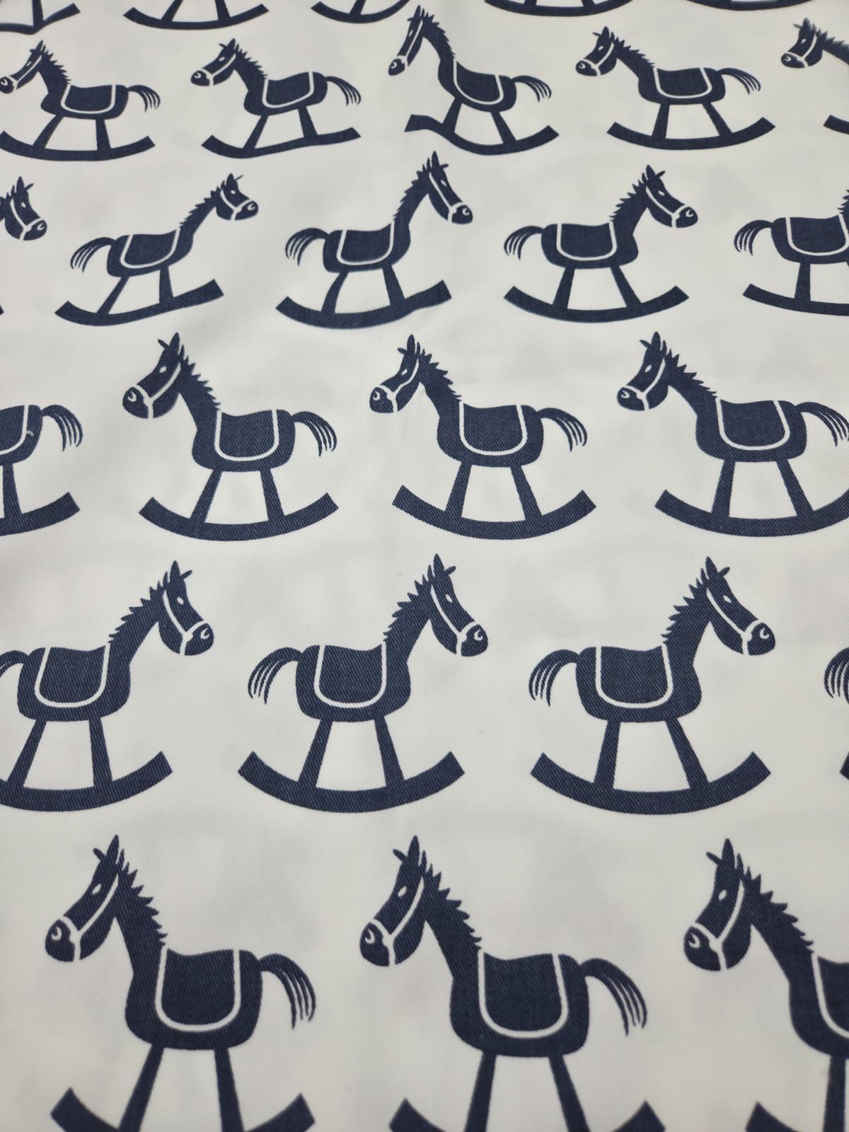 Pattern of navy blue rocking horses on white fabric in repeating rows creating a classic nursery print design.