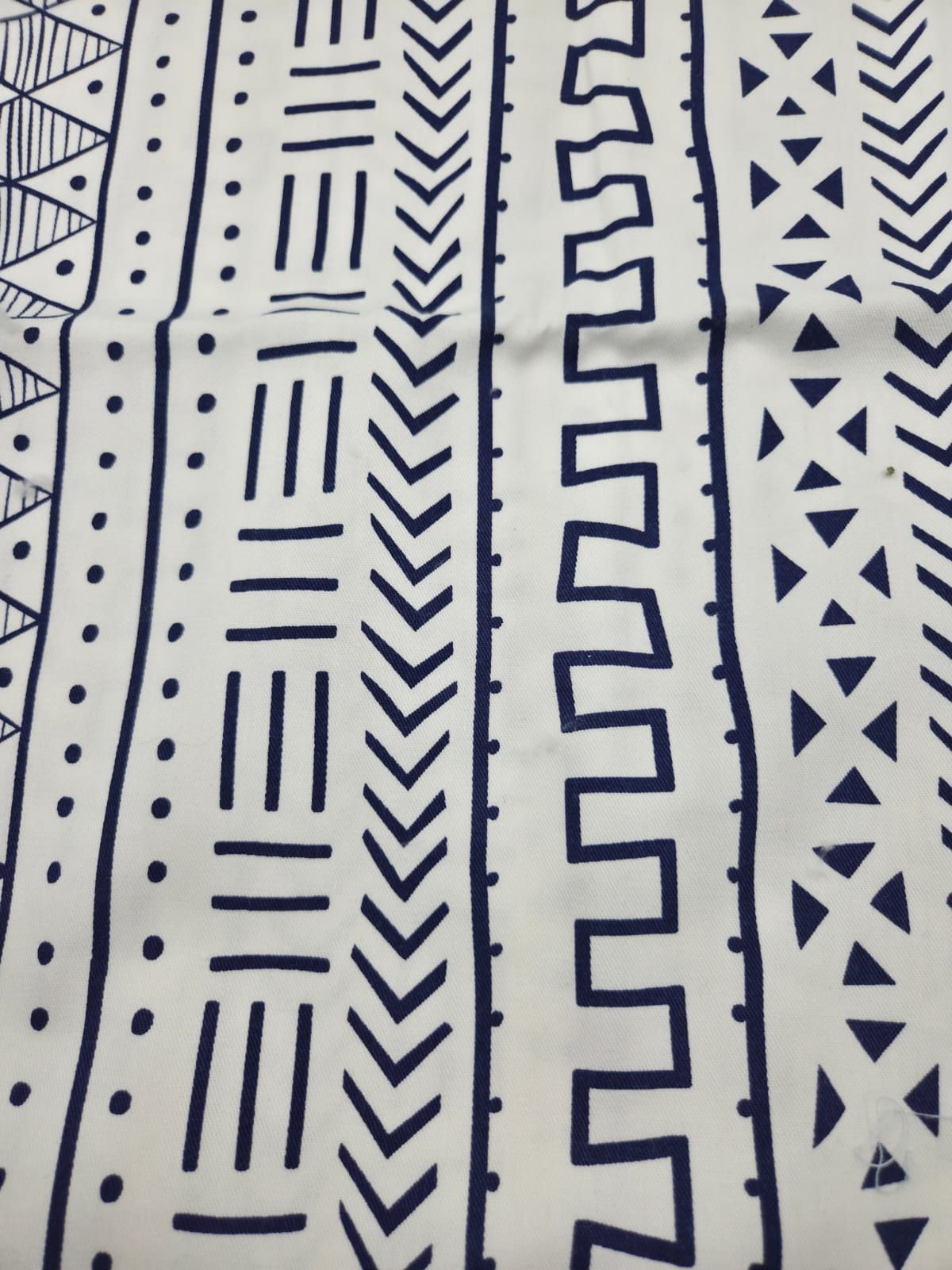 Abstract geometric pattern featuring navy blue tribal-inspired lines, dots, and zigzag shapes on a light background.