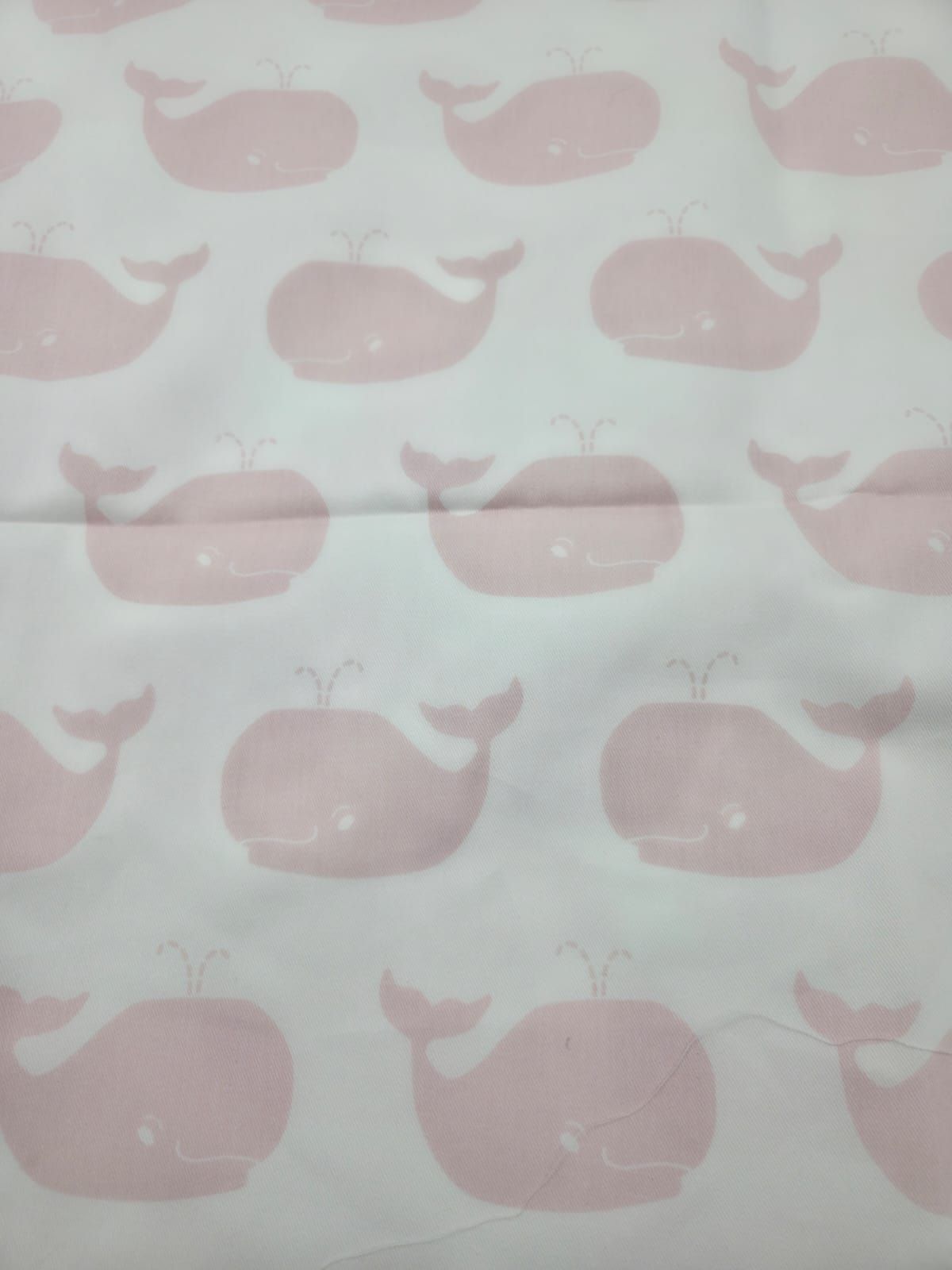 Light pink whale silhouettes repeated on white fabric creating a delicate nautical pattern.