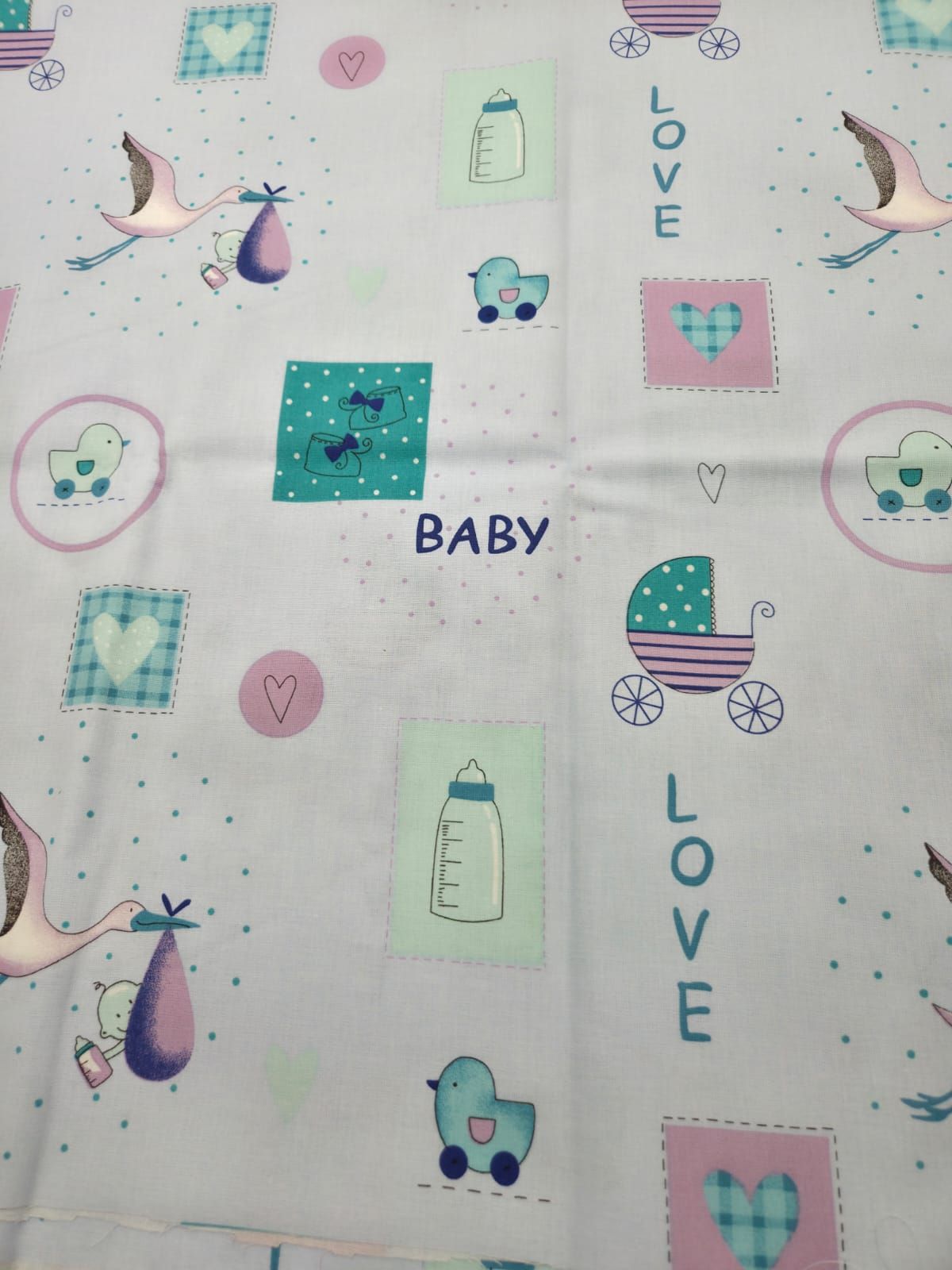 Baby-themed fabric pattern with storks, baby bottles, hearts, and strollers in soft pink and turquoise colors on white background.