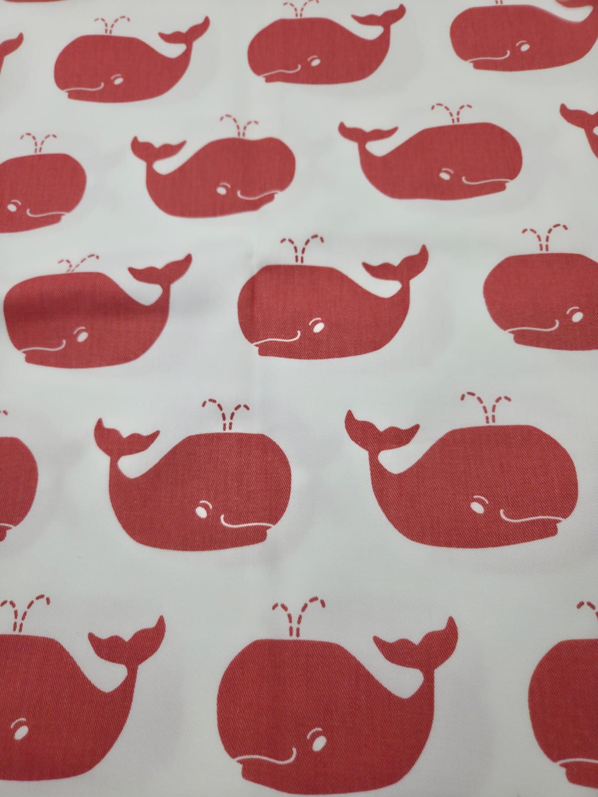 Repeating pattern of red whales with white eyes on a white background creating a playful nautical design.