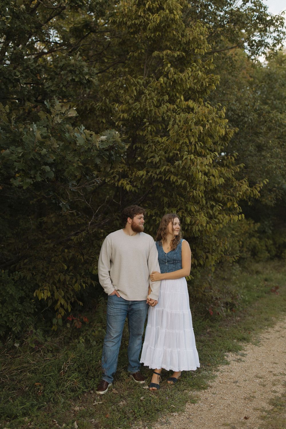 A couple walks together on a dirt path surrounded by autumn trees and foliage.