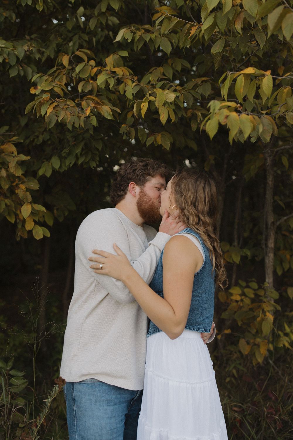 A couple shares an intimate moment among fall foliage in a wooded setting.