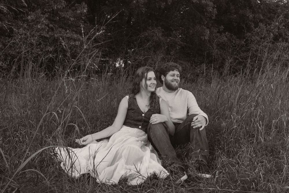 A couple relaxes together in a field with tall grass and natural lighting.