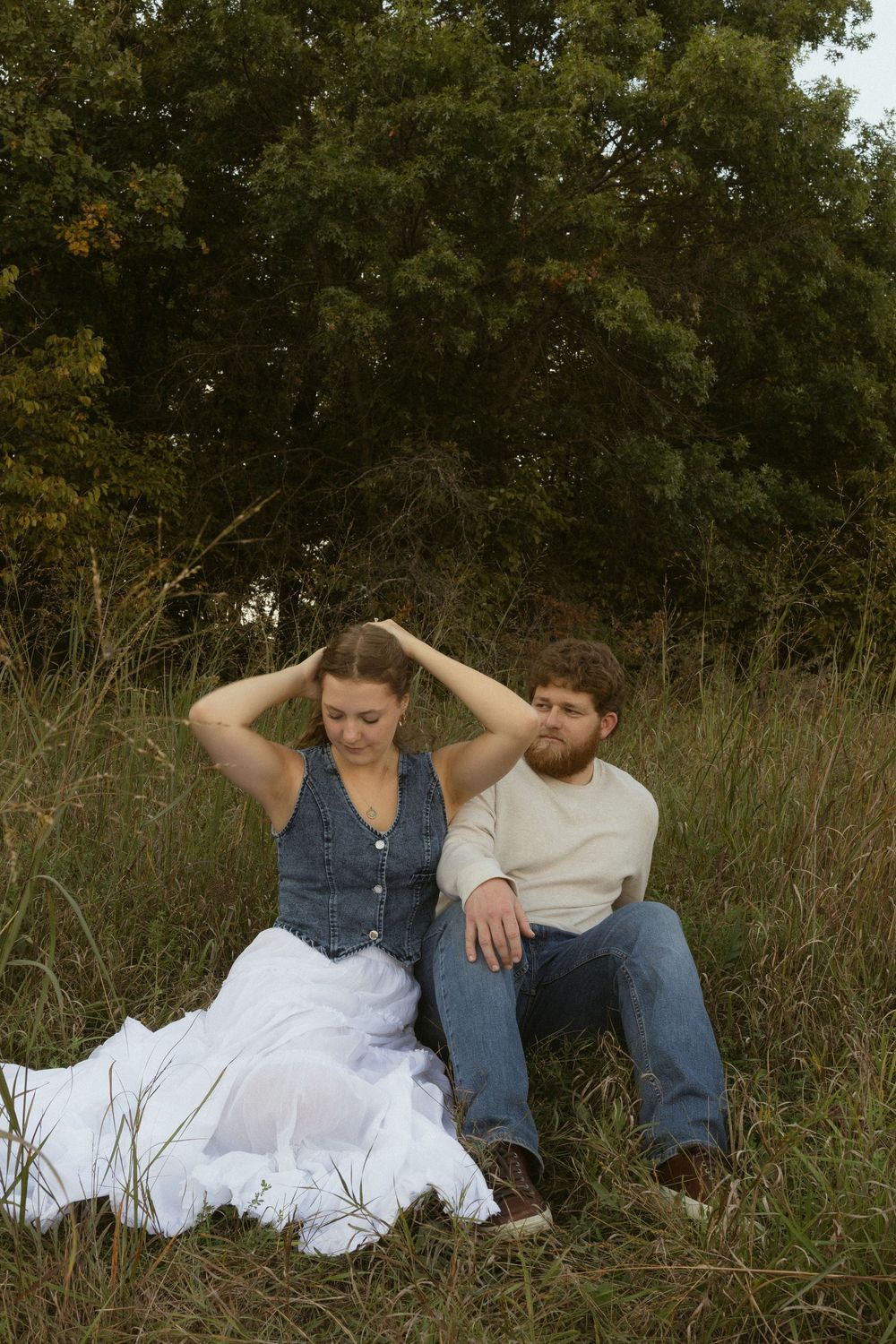 A couple lounges casually in tall grass during an outdoor photo session.