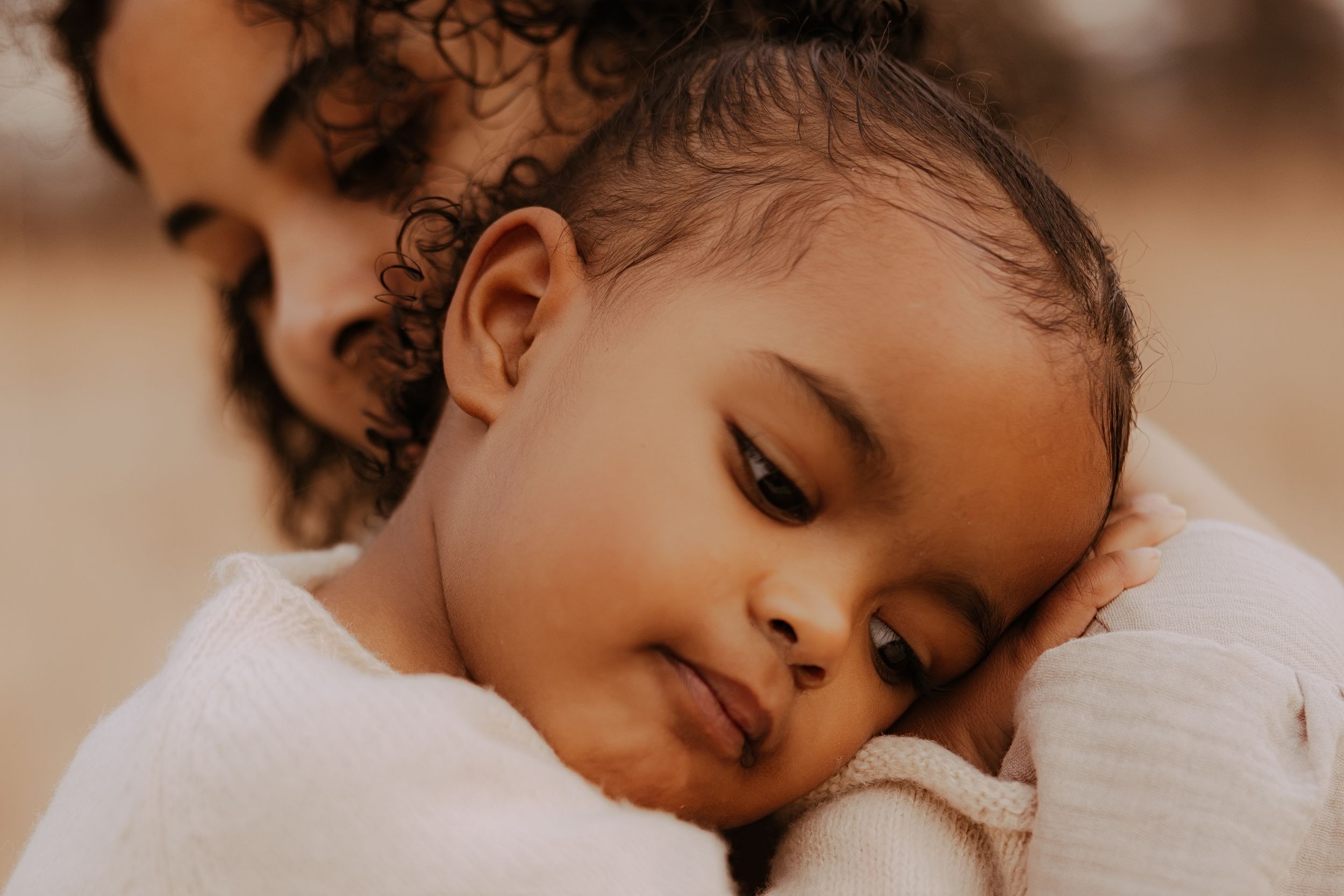 A sleeping baby rests peacefully in a cozy white blanket with natural lighting creating a warm, serene atmosphere.