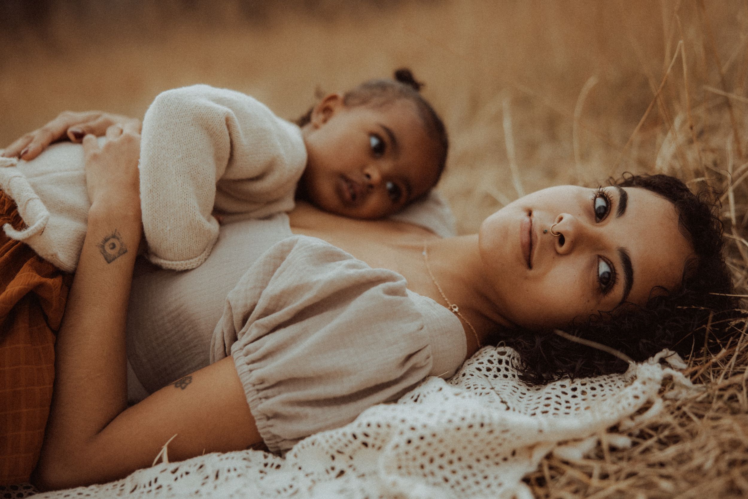 Two people lying together in a field of golden grass during sunset in warm earthy tones.
