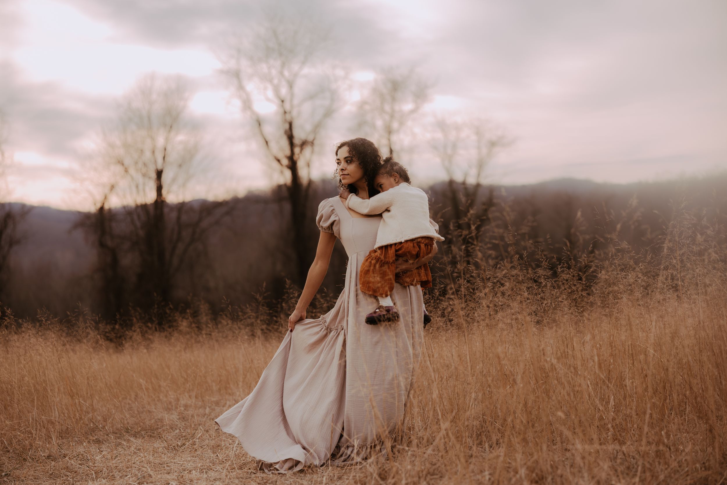 Person in flowing white dress stands gracefully in golden autumn field during moody overcast sunset.