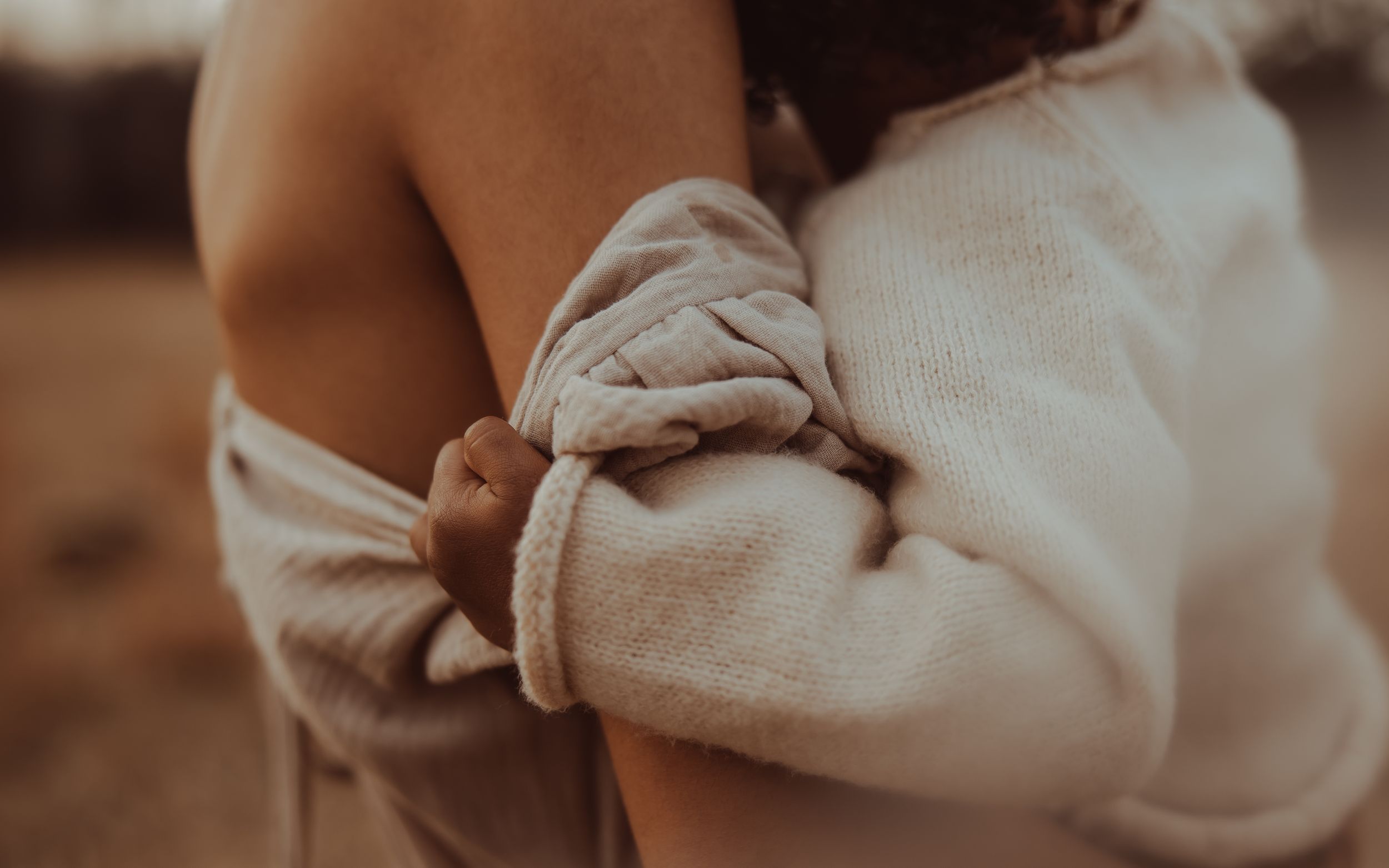 Cropped collage of hands holding a small baby wearing a white onesie in warm, sepia-toned lighting.