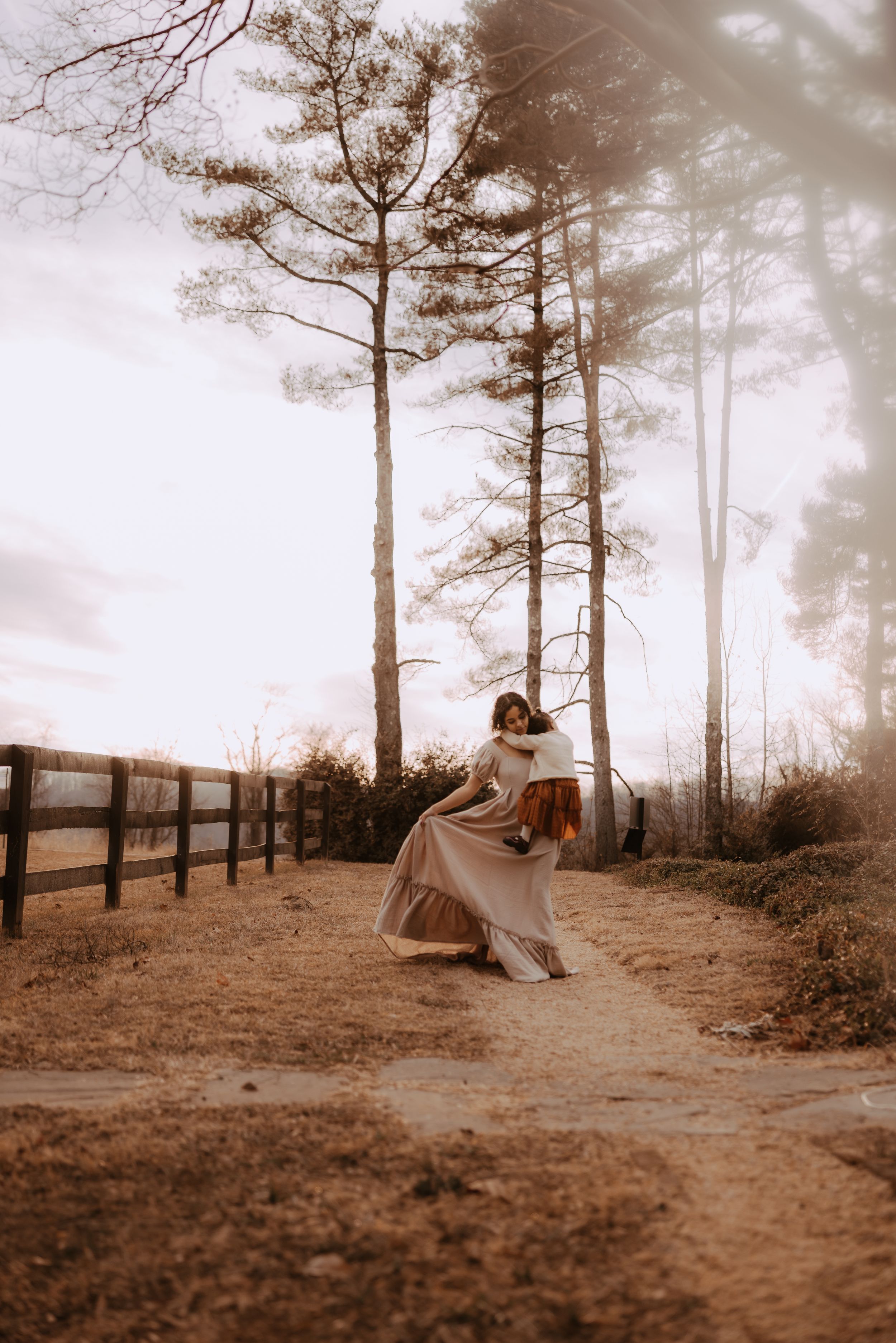 Sepia toned sequence showing a figure in flowing dress walking along a rustic fence line with pine trees.