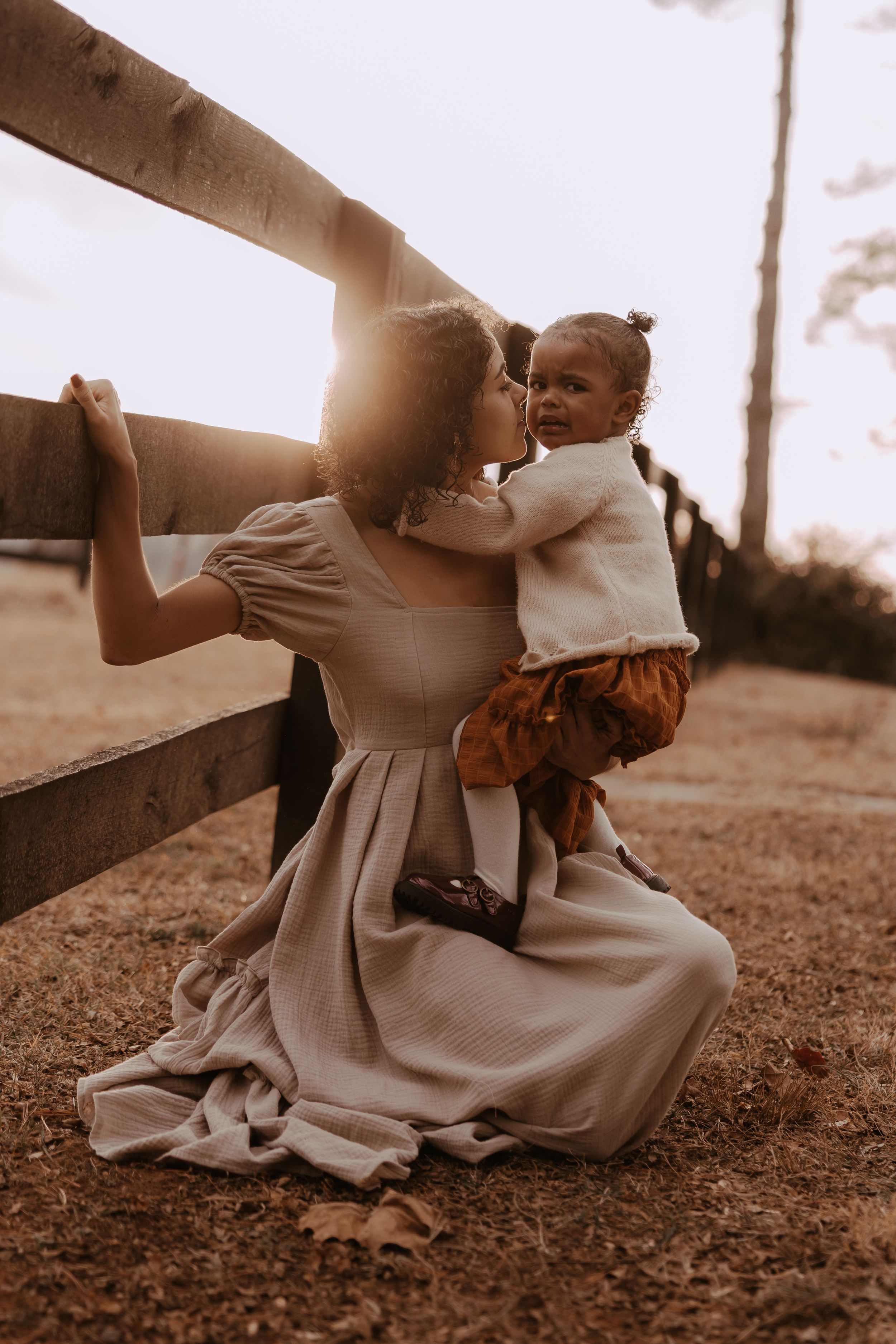 A vintage-style scene shows someone in a long dress sitting on the ground in warm sepia tones at sunset.