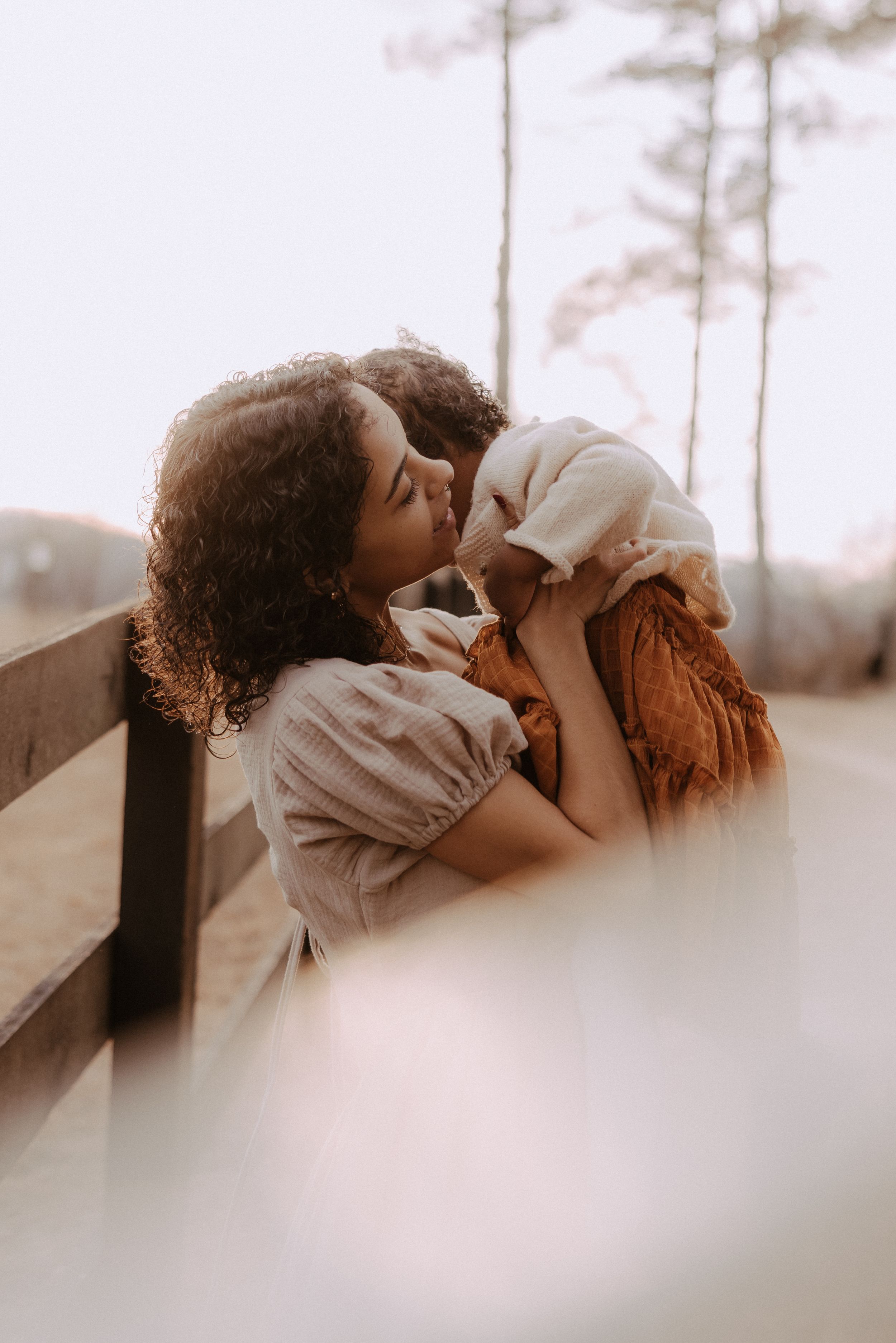 A romantic couple sharing intimate kisses in a dreamy outdoor setting with pine trees in the background.