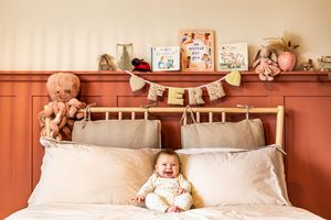 Happy baby sitting on a bed beneath a personalized name banner and shelf with toys and books.
