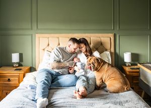 Happy family with tattooed father, mother, newborn baby, and bulldog relaxing on bed.