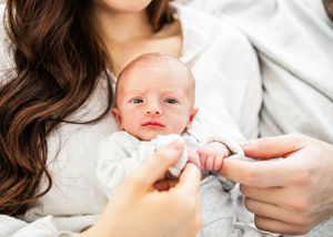 Close-up of newborn baby being cradled in mother's arms with tiny hands visible.